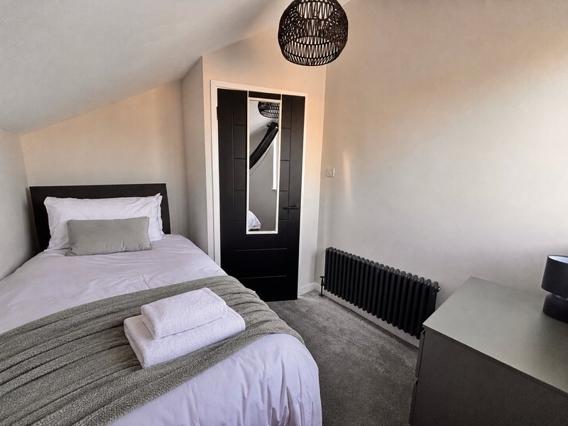 Bedroom with single bed, grey bedding, black door and woven ceiling pendant light