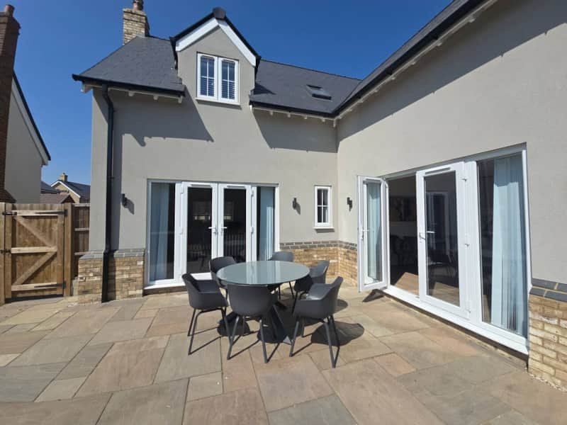 Modern house exterior with patio, outdoor dining table and chairs, clear blue sky