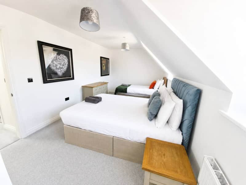 Bright attic bedroom with two beds, blue headboard, framed wall art, and sloped ceiling