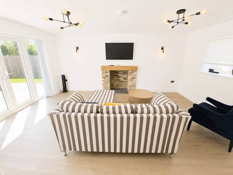 Modern living room with striped sofa, fireplace, wall-mounted TV, and garden doors