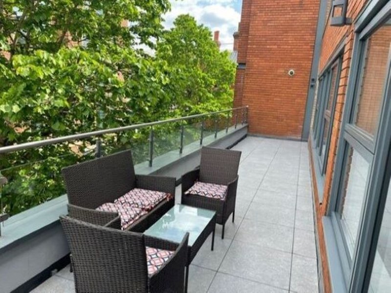 Modern brick building balcony with rattan seating, glass table, and green foliage views