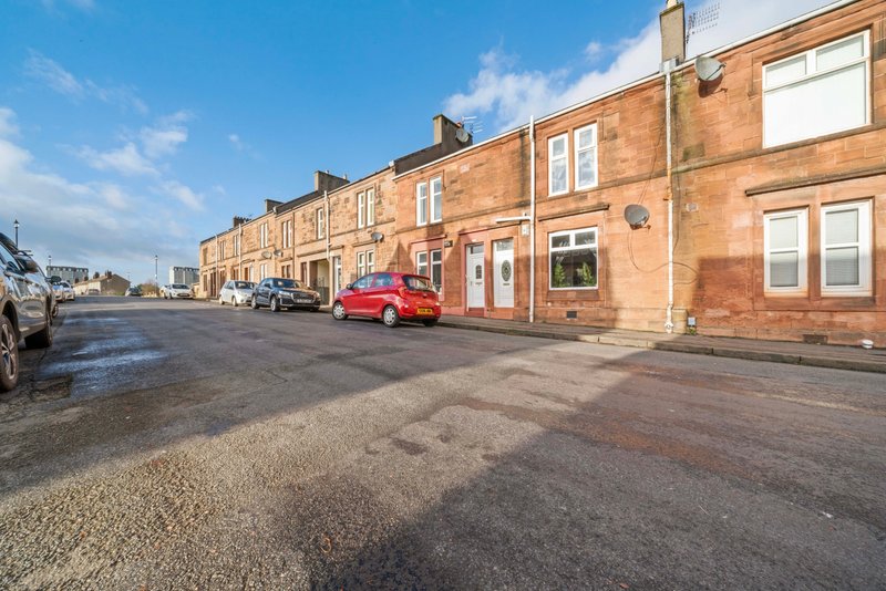 Street-facing red-brick residential building with parked cars and clear sky