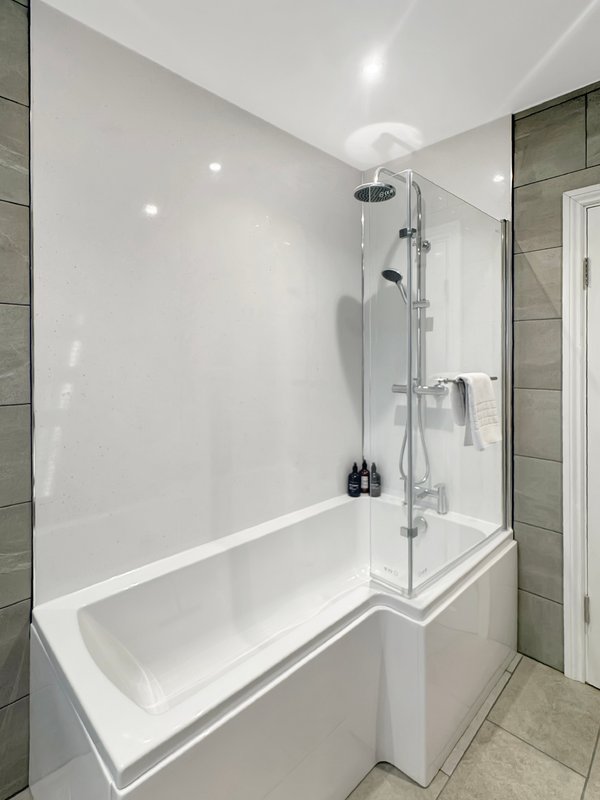 Modern bathroom with white bathtub, glass shower enclosure and grey tile walls