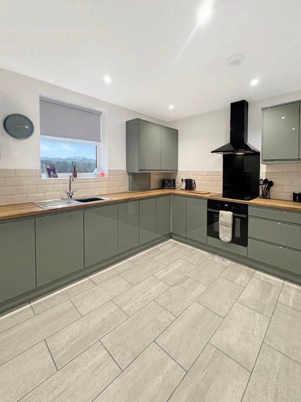 Modern kitchen with sage green cabinetry, wooden worktops, black range hood and tiled flooring