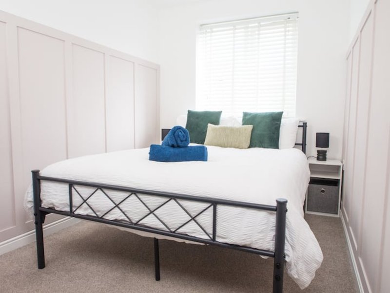 Bedroom with metal-framed bed, white bedding, green pillows, blue towels, and built-in wardrobes