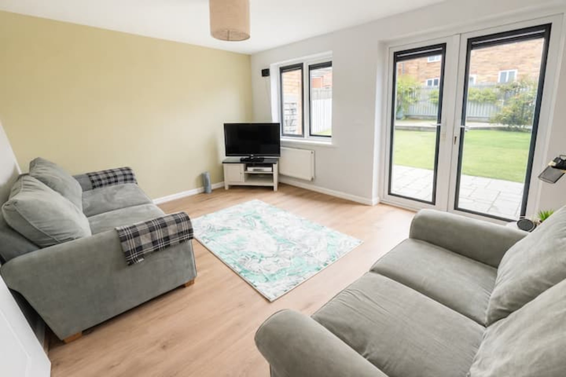 Bright living room with grey sofas, TV, patterned rug and glass doors to garden