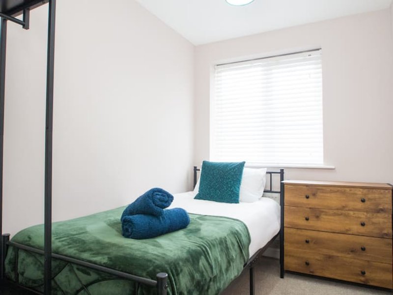 Bedroom with single bed, green bedding, rolled towels, wooden dresser and window