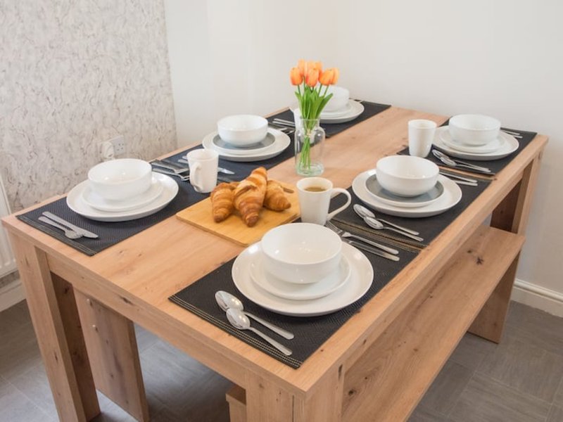 Dining table set with white plates, black placemats, orange tulips and croissants