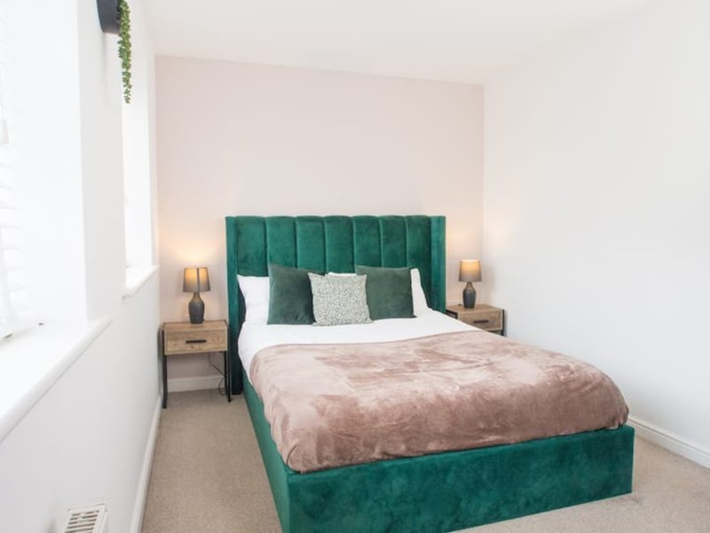 Bedroom with green velvet bed, white bedding, pink throw, and wooden nightstands