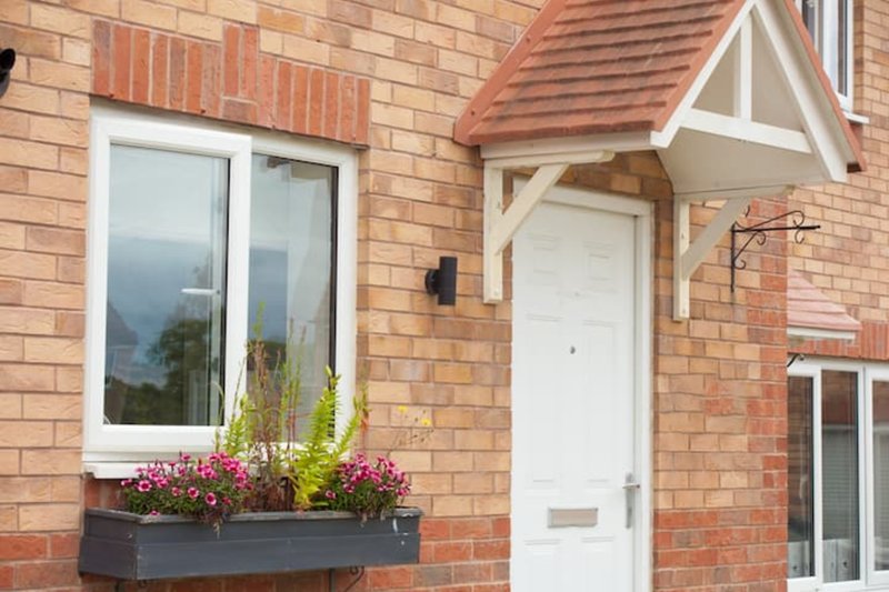 Brick house exterior with white door, window, and flowering window box planter