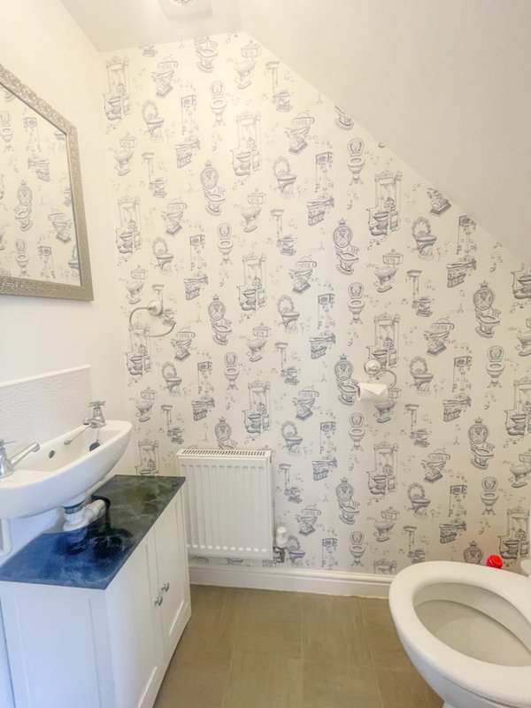 Bathroom with patterned wallpaper, white sink vanity, toilet, and radiator