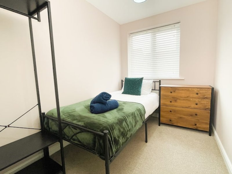 Bedroom with single bed, green bedding, wooden dresser and window with blinds