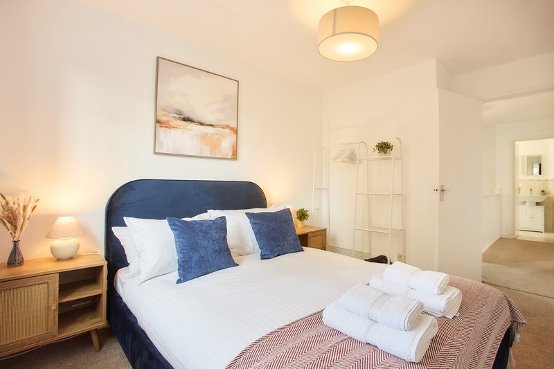 Modern bedroom with blue upholstered bed, white bedding, blue cushions and rolled towels