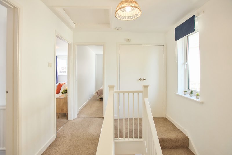 Bright hallway with white doors, wooden gate, carpet flooring and pendant ceiling light