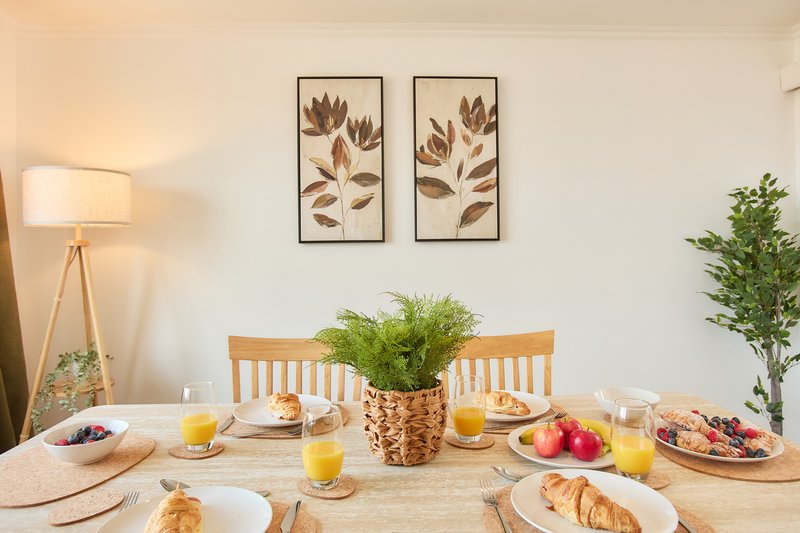 Dining table set for breakfast with fruit, pastries, juice and floral wall art