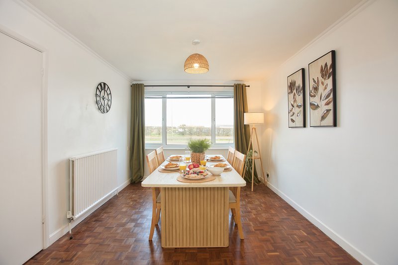 Dining room with wooden table, green curtains, large window overlooking countryside, pendant light