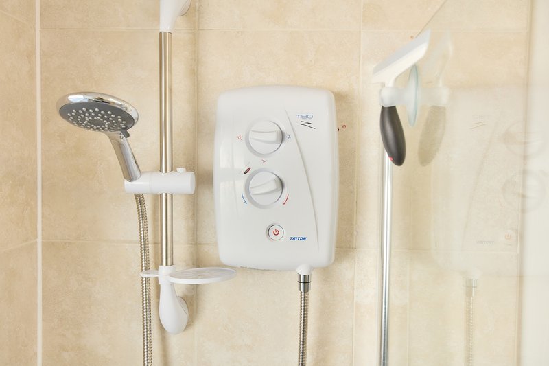 Bathroom shower with electric heating unit, showerhead, and handheld spray on tiled wall
