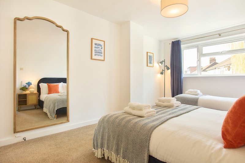 Bright bedroom with twin beds, large mirror, window with curtains and orange accent pillows