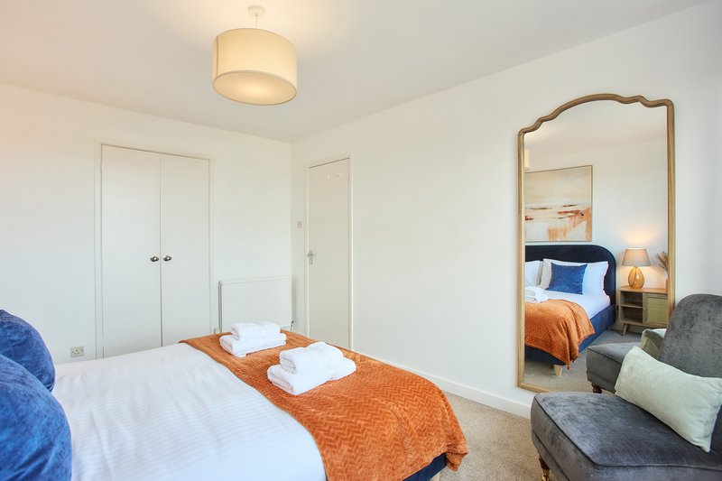 Modern bedroom with double bed, orange throw, white pillows, large mirror and seating area