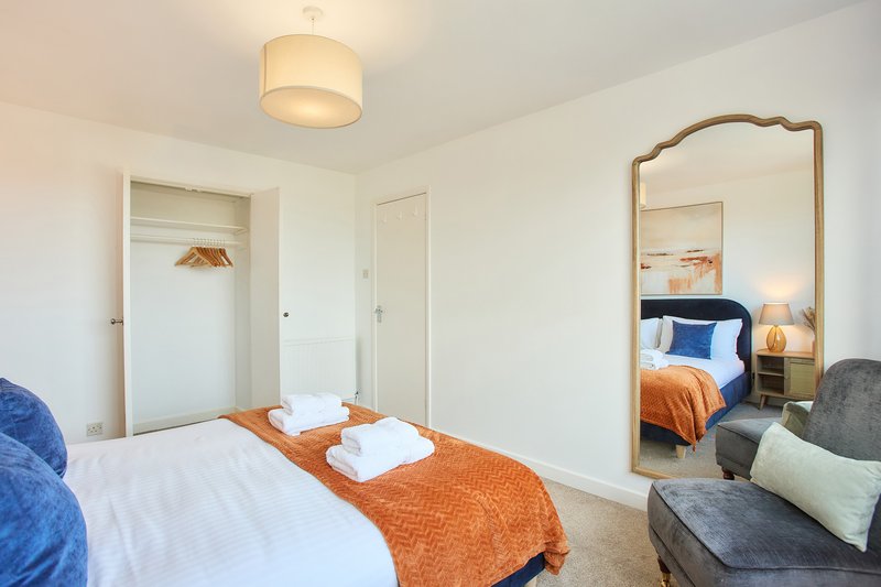 Bright bedroom with two beds, orange throw, large mirror, closet and seating area