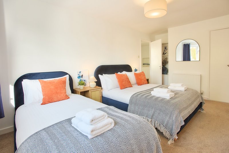 Twin bedroom with two beds, orange cushions, white towels, and cream walls