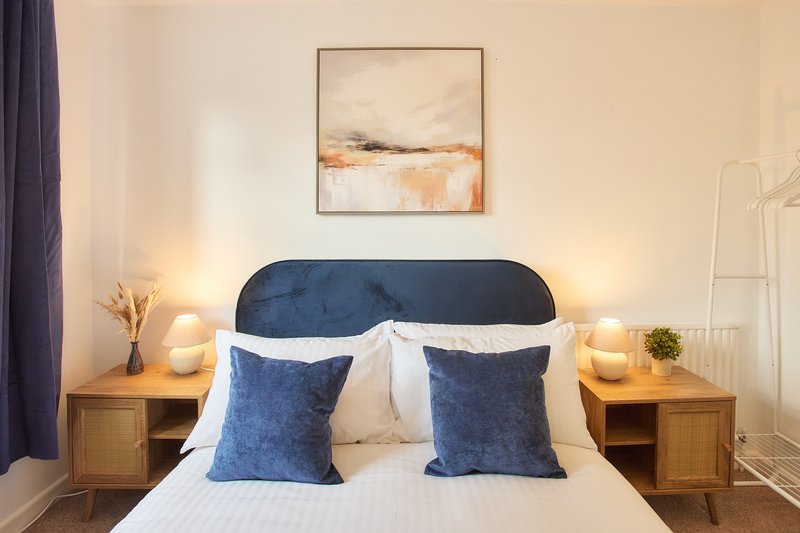 Modern bedroom with blue upholstered headboard, white bedding, blue cushions and wooden nightstands