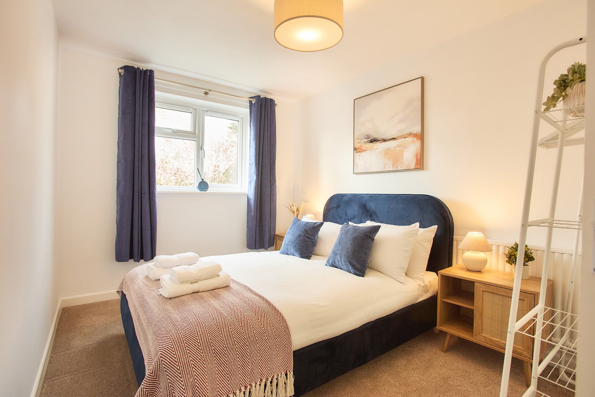 Modern bedroom with double bed, navy headboard, cushions, and folded towels on foot rail