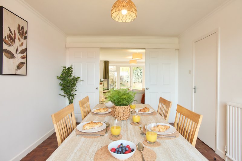 Bright dining room with wooden table set for four, pendant light, framed wall art, potted plant