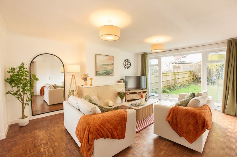Bright living room with two cream sofas, orange throws, wooden floor and garden view