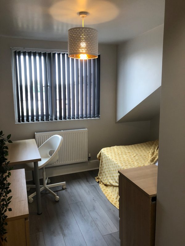 Bedroom with single bed, desk, chair, pendant light and vertical blinds