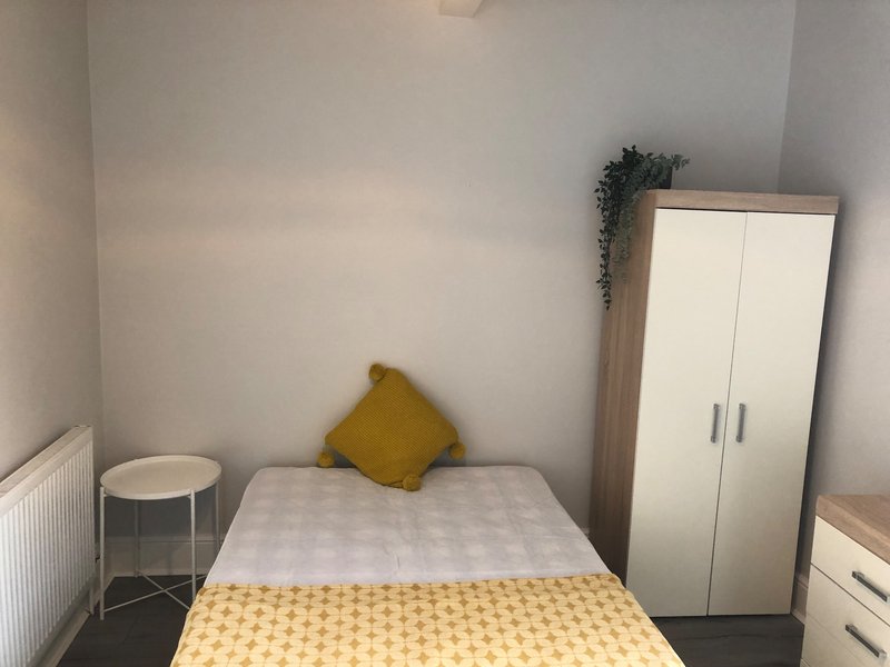 Small bedroom with single bed, yellow bedding, mustard cushion, wardrobe and side table