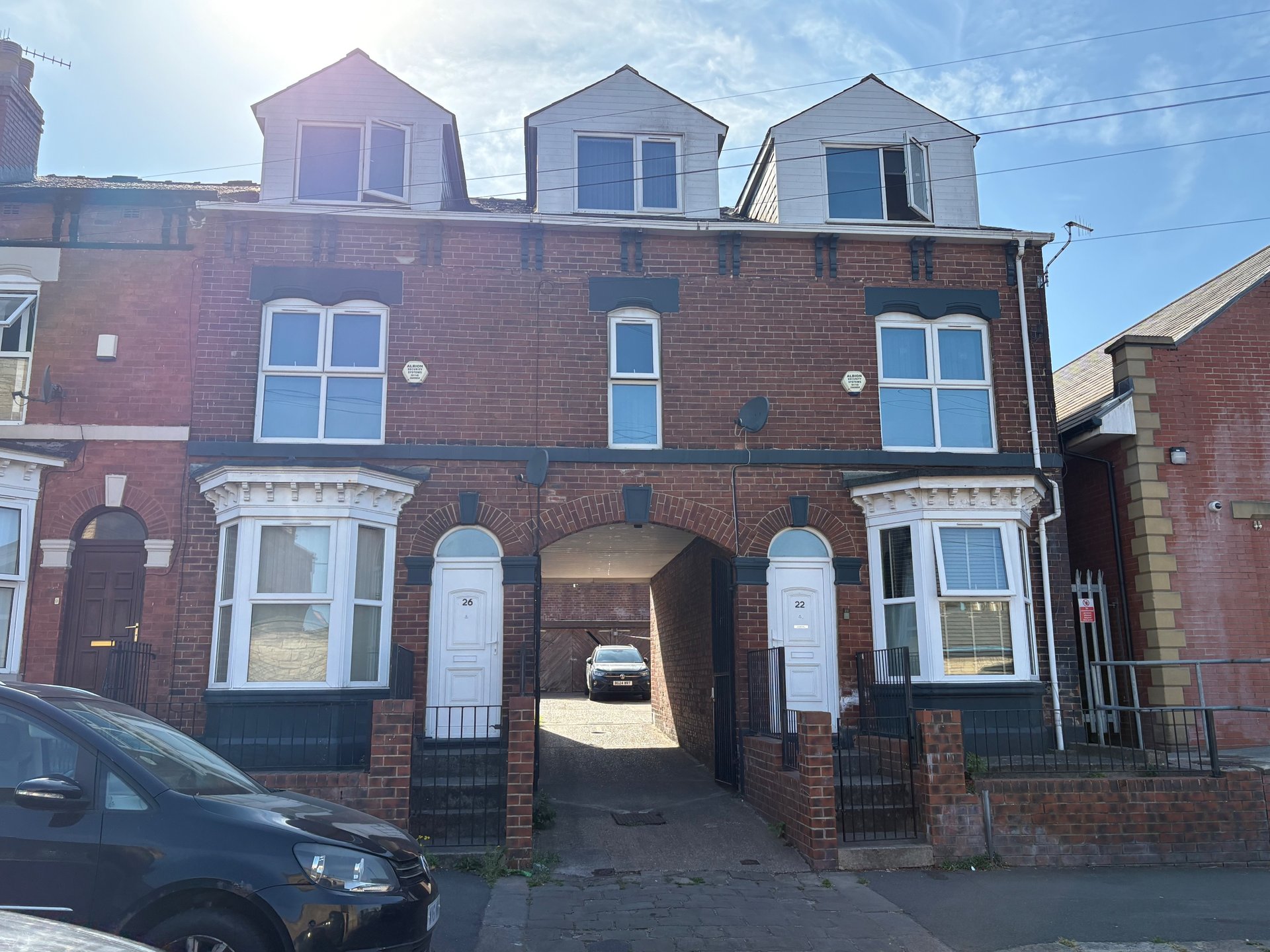 Red brick terraced house with three dormer windows, arched passageway, and parked car