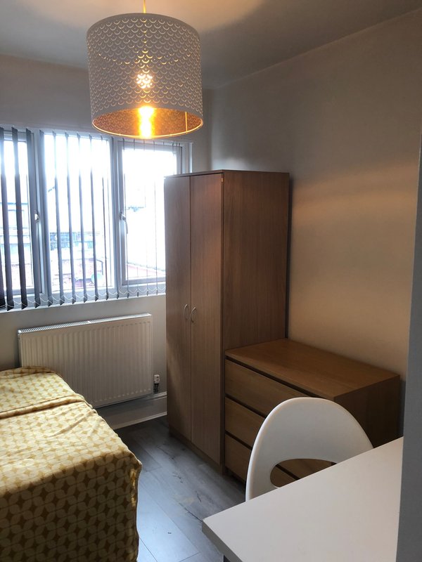 Bedroom with single bed, wooden wardrobe, desk chair, pendant lamp and vertical blinds