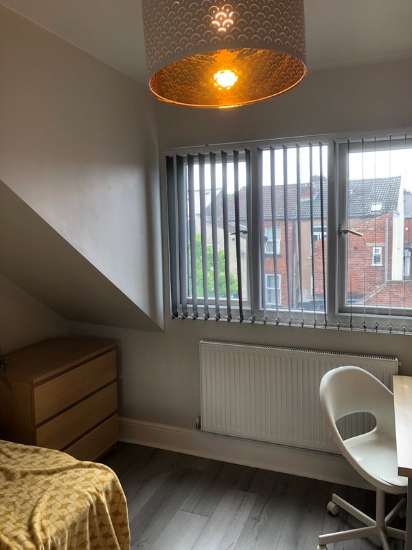 Bright bedroom with double bed, wooden dresser, pendant lamp, and large window overlooking street