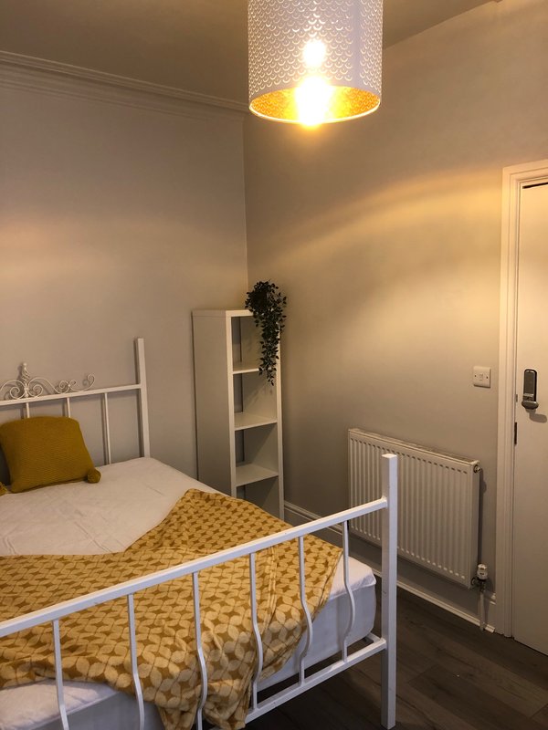 Bedroom with white metal bed frame, yellow bedding, ceiling lamp, white shelving unit, and radiator