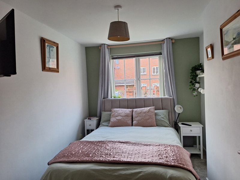 Compact bedroom with double bed, sage green accent wall, window with curtains and street view