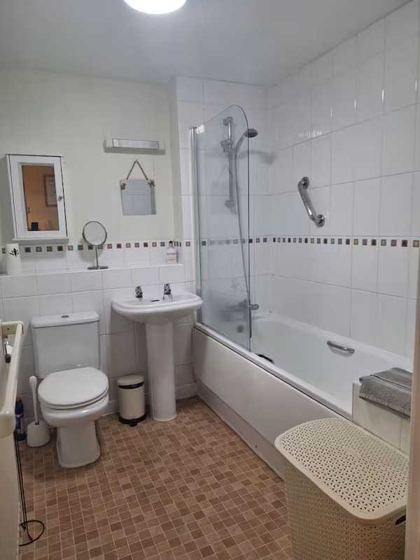 Bathroom with toilet, pedestal sink, bath with glass shower screen and tiled walls