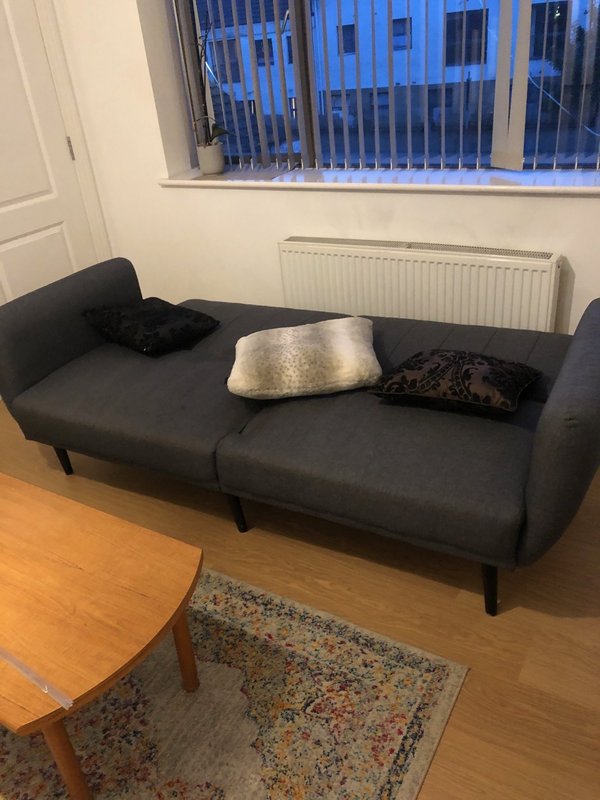 Modern living room with black sofa, wooden table, radiator and large window with blue blinds