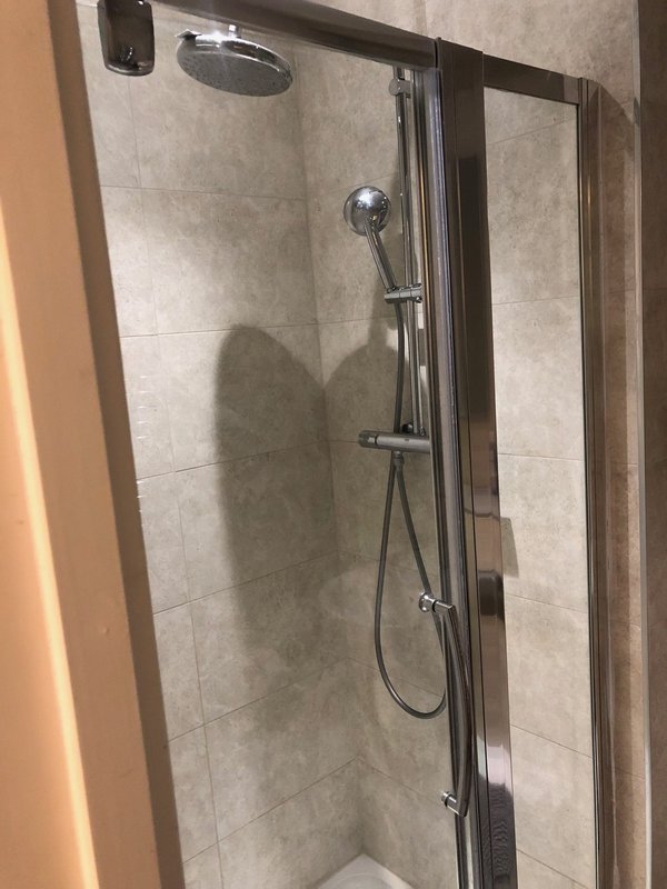 Modern bathroom shower enclosure with rainfall and handheld showerheads, tiled walls