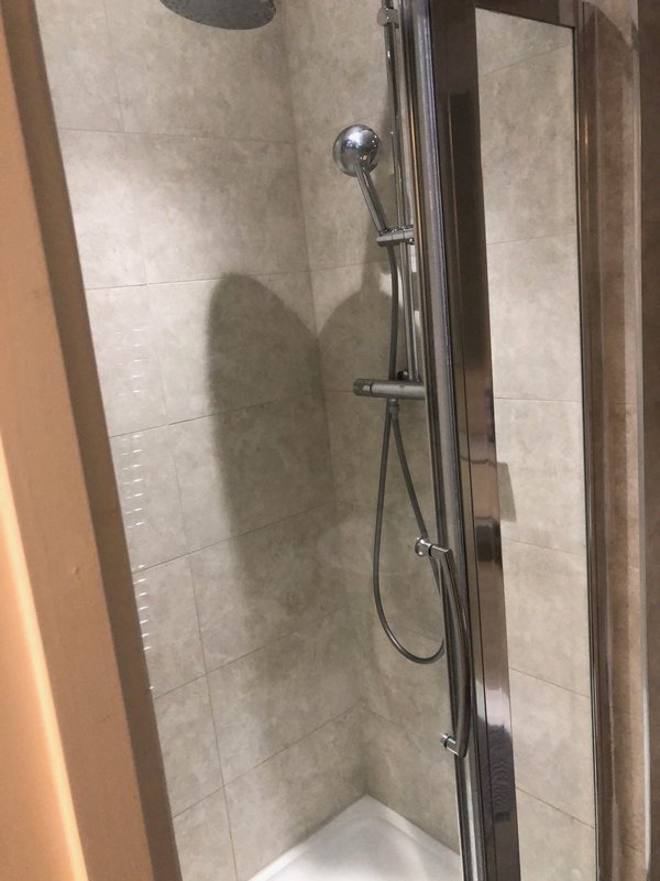 Bathroom shower enclosure with tiled walls, chrome showerhead and handheld spray