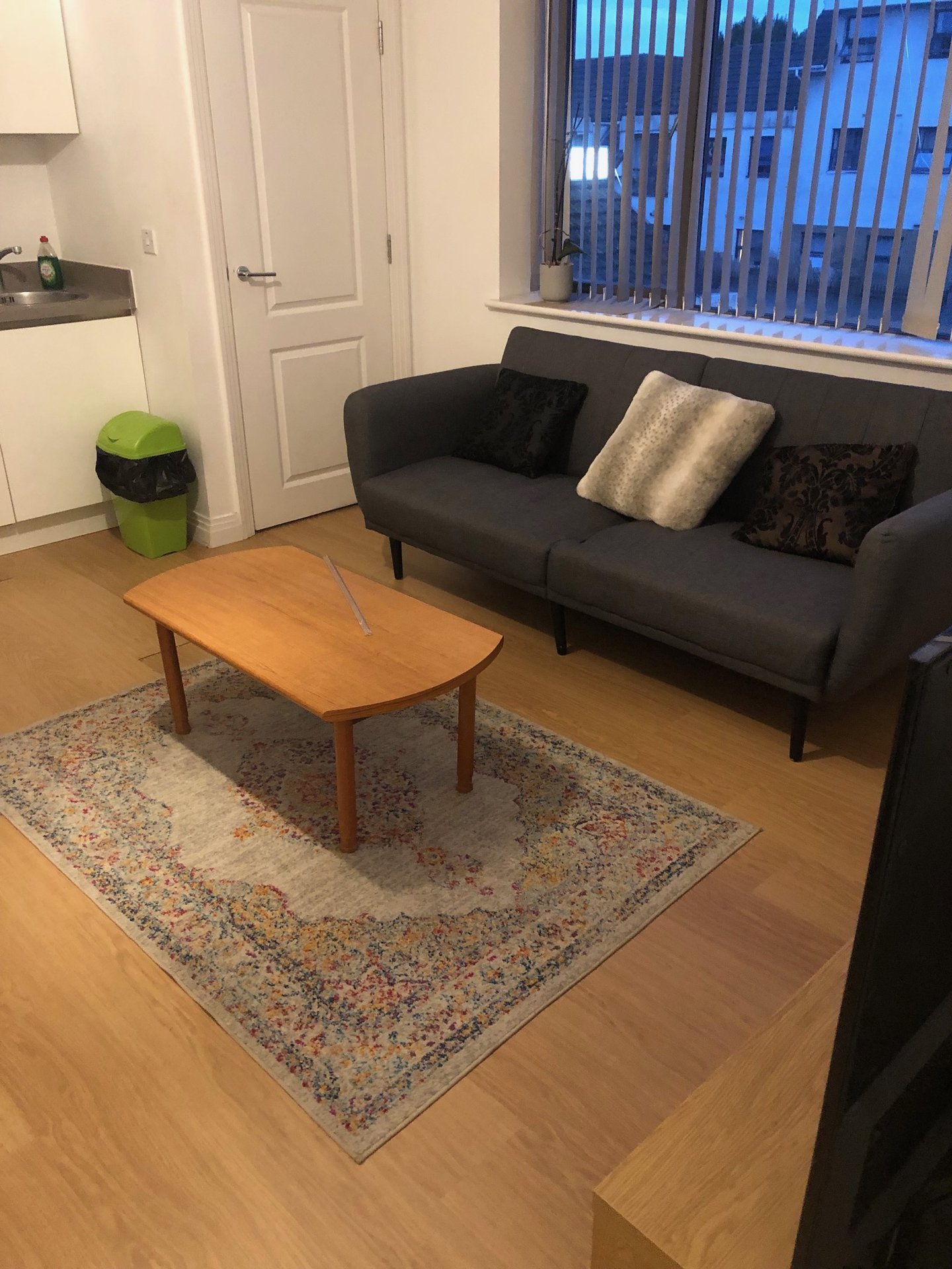 Living room with black sofa, wooden coffee table, area rug, and large window with blinds