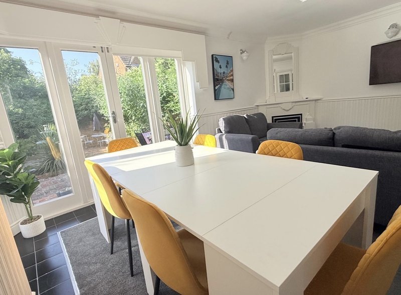 Open-plan living and dining area with white table, mustard chairs, dark sofa, and garden access through patio doors