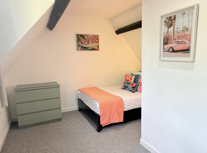 Attic bedroom with single bed, orange throw, green dresser and framed wall art