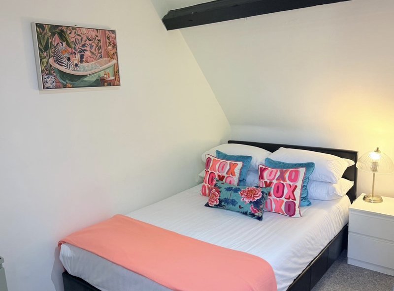 Attic bedroom with double bed, colorful cushions, wall art and bedside lamp