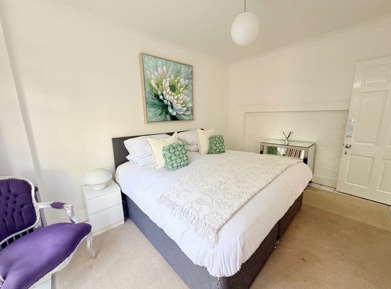 Bright bedroom with double bed, purple accent chair, wall art, and wooden flooring