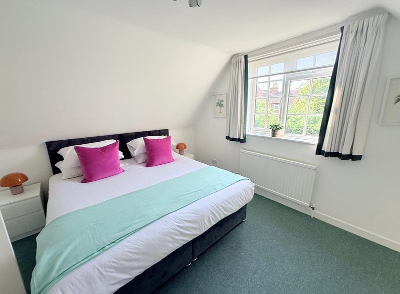 Bright bedroom with double bed, pink cushions, mint green throw, and large window with curtains
