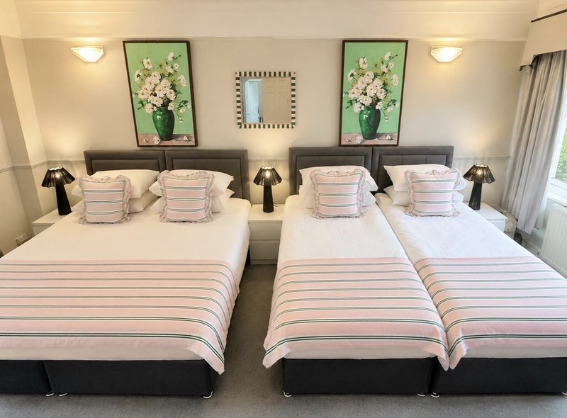 Bright bedroom with two double beds, striped bedding, framed flower artwork, and bedside lamps
