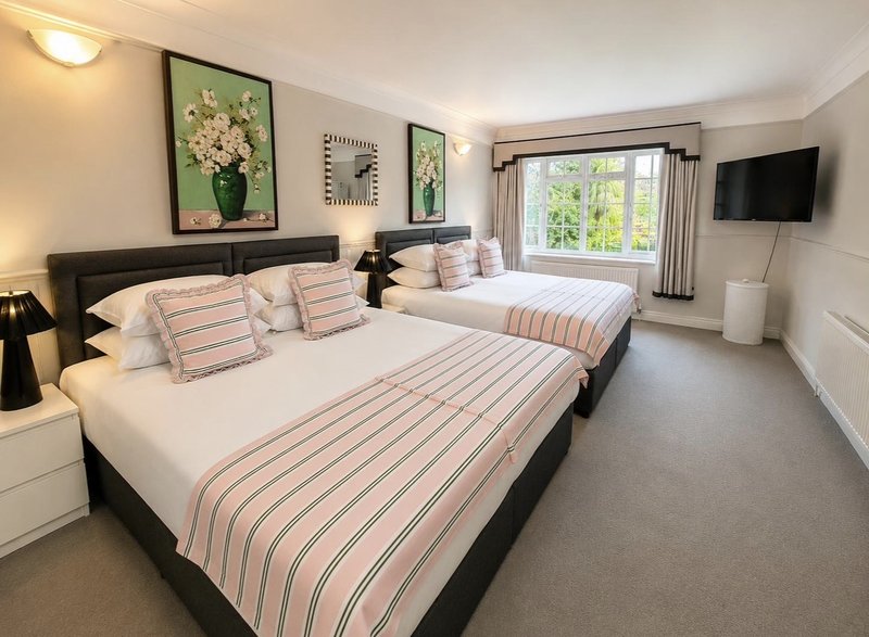 Bright bedroom with two double beds, striped bedding, framed artwork, and large window with garden view