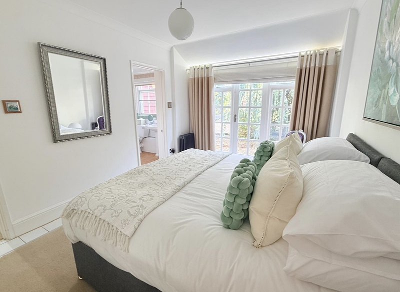 Bright bedroom with double bed, white bedding, green cushions, mirror and garden view