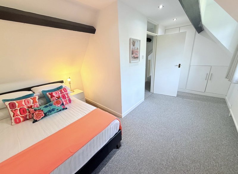 Bright bedroom with double bed, colorful cushions, bedside lamp, and open door to hallway